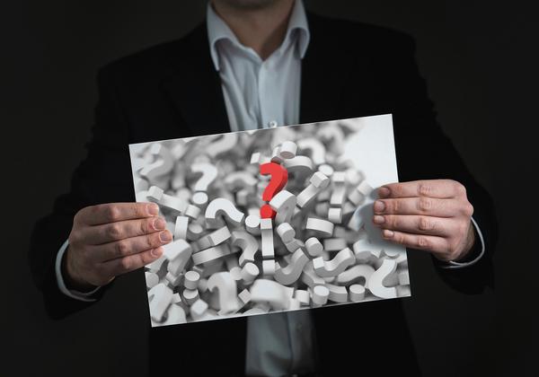 Person holding a sign with question marks, with a red question mark in the middle